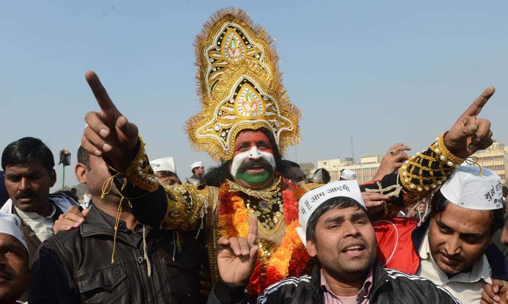 Supporters of the anti-corruption champion and Aam Admi Party (one dressed as Hindu Lord Rama) watch their unseen leader Arvind Kejriwal taking his oath of office as Chief Minister of India's national capital region from Delhi's Lt. Governor.