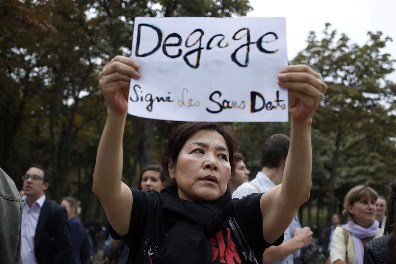 A demonstrator holds a placard reading "Get out, signed by the toothless" 
