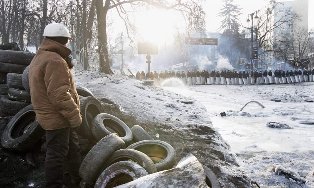 A protester sits behind a barricade of tires as riot police stands in line during another day of anti-government protest in Kiev, Ukraine, 27 January 2014. (AAP)