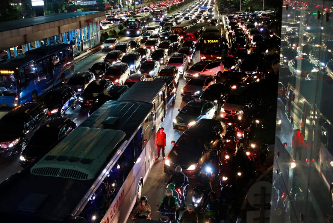 A city bus crew member stands next to his vehicle as he is illuminated red by the tail lights of other vehicles in rush hour traffic in Jakarta, Indonesia, Friday, May 19, 2017 (AAP)