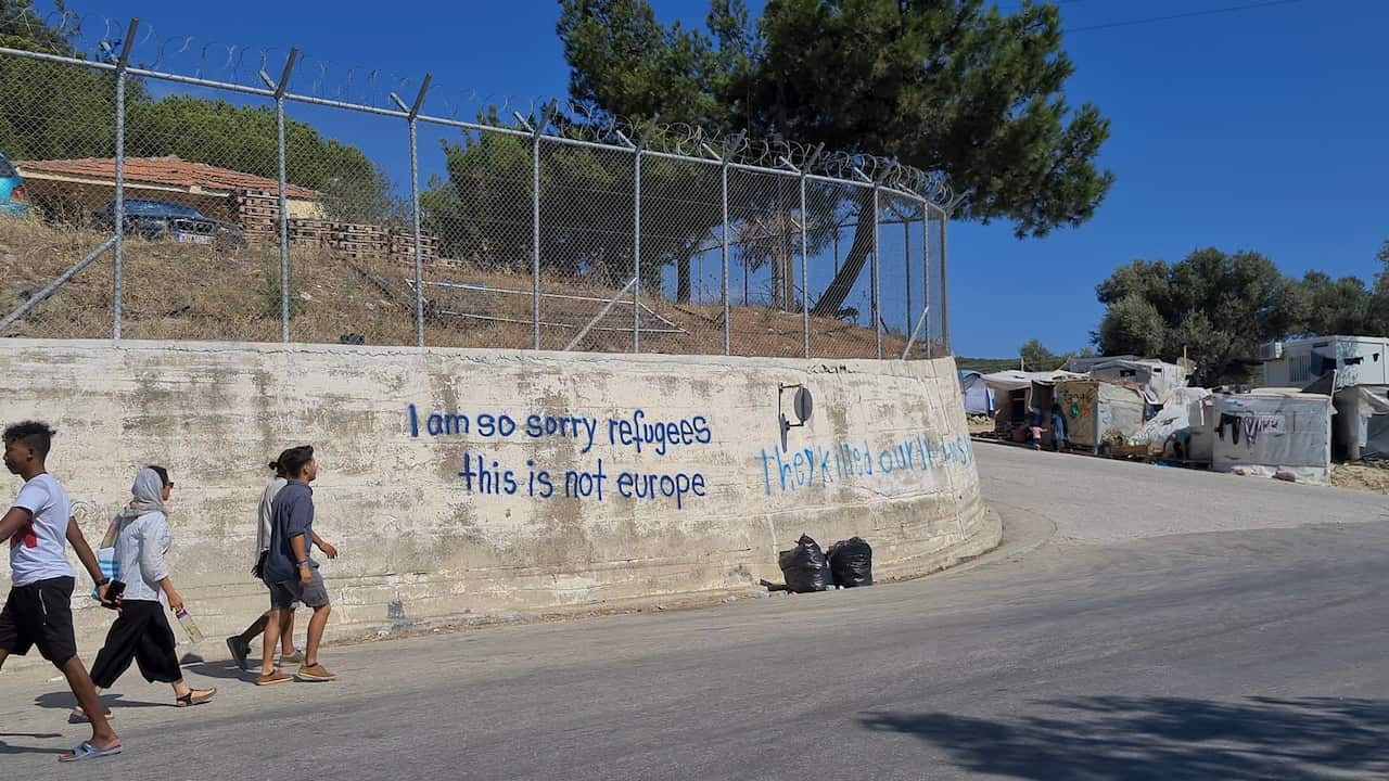 Asylum seekers walk past a sign at the Moria Refugee Camp on Lesbos island, Greece.