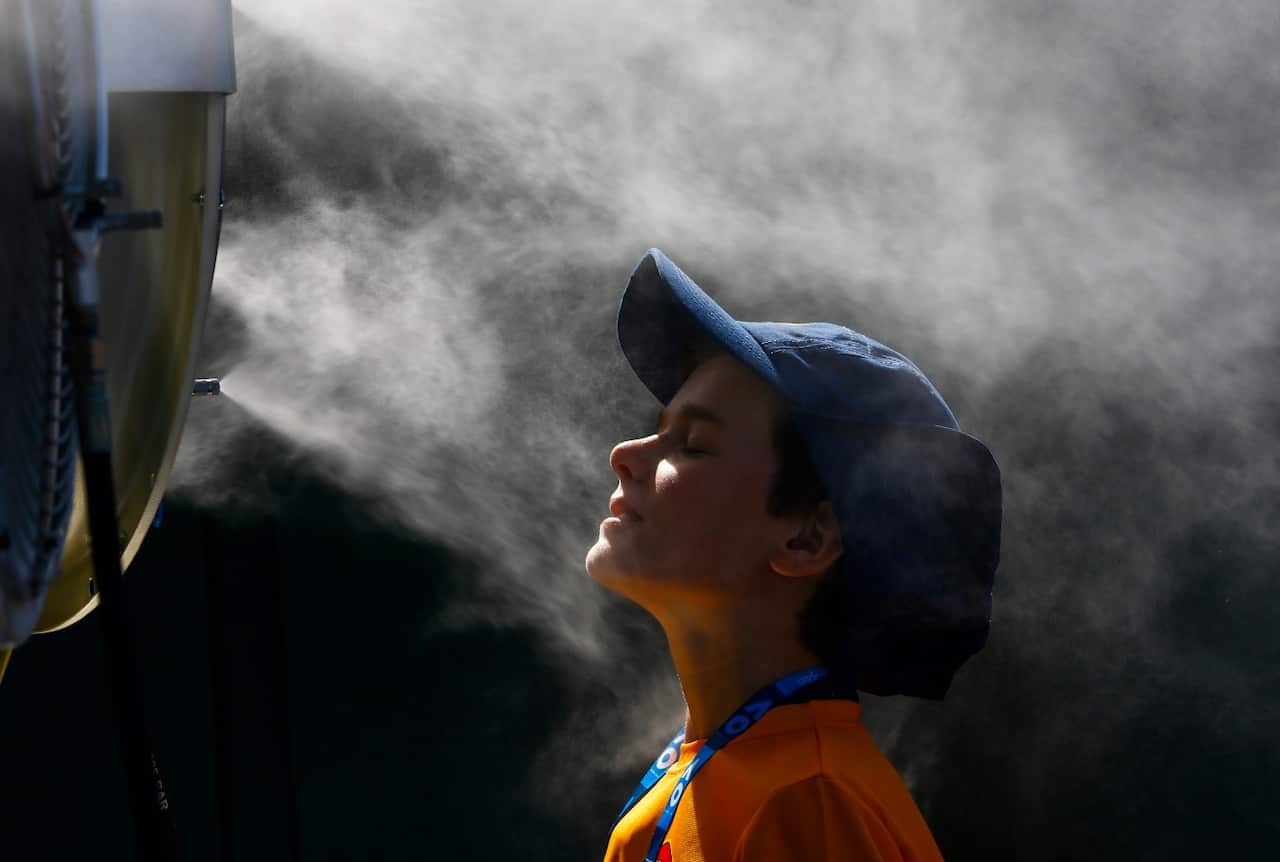 A ball boy cools off in mist sprayed by a water misting fan on a hot summer day at the Australian Open tennis tournament in Melbourne, Australia (AAP)