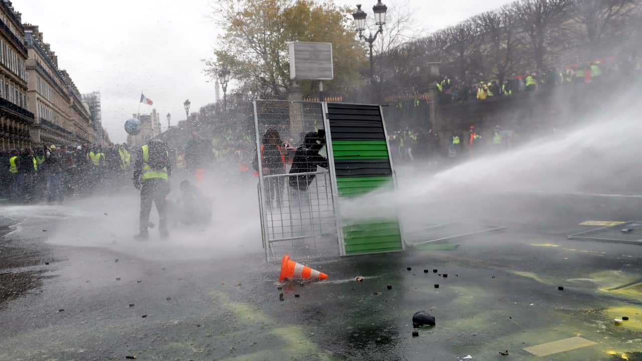 Demonstrators use street barriers to shield from water cannons during a demonstration in Paris.