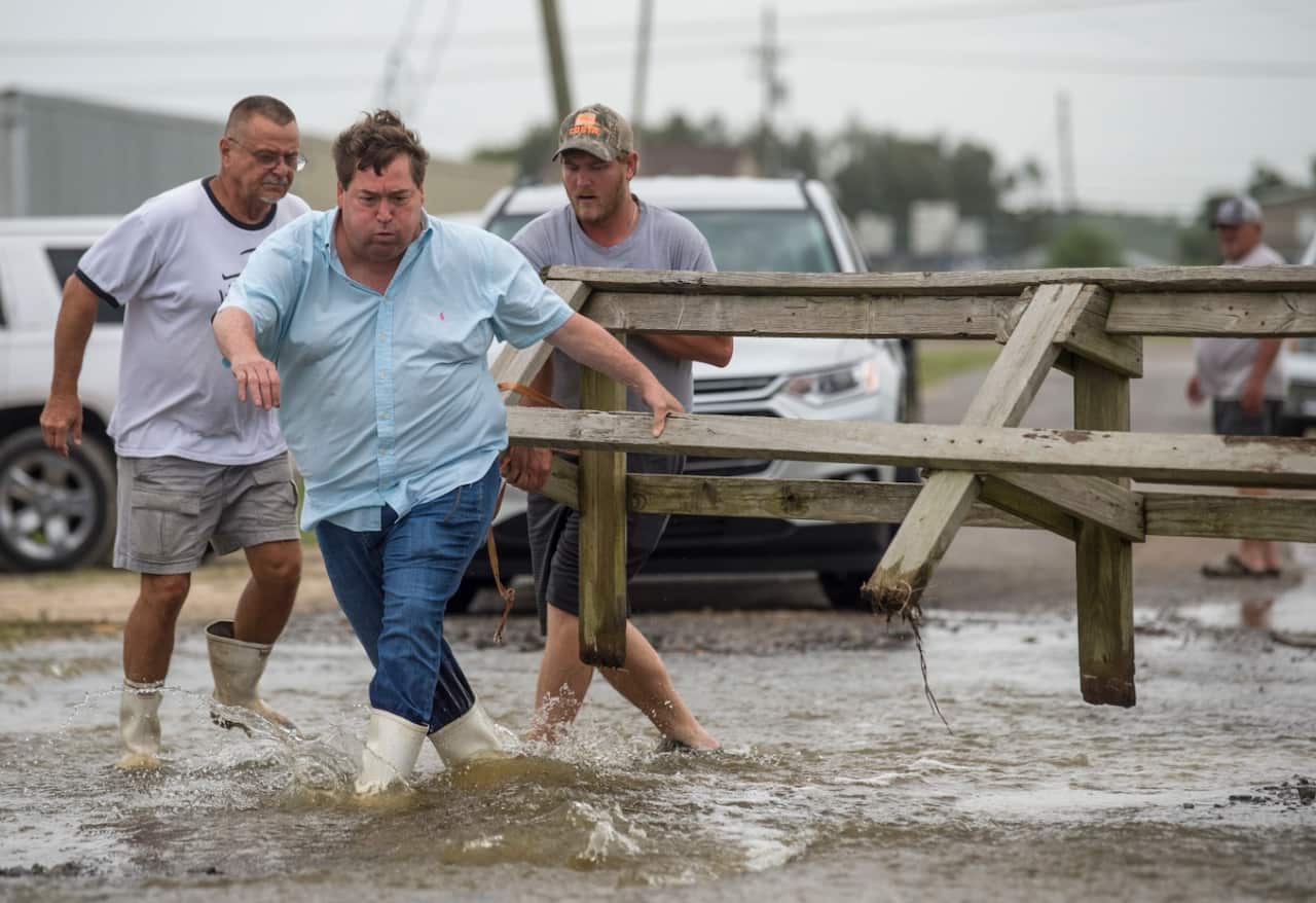 Louisiana Lt. Gov. Billy Nungesser, left center, helps move a wooden barricade to block a road where water was rising in Plaquemines Parish 