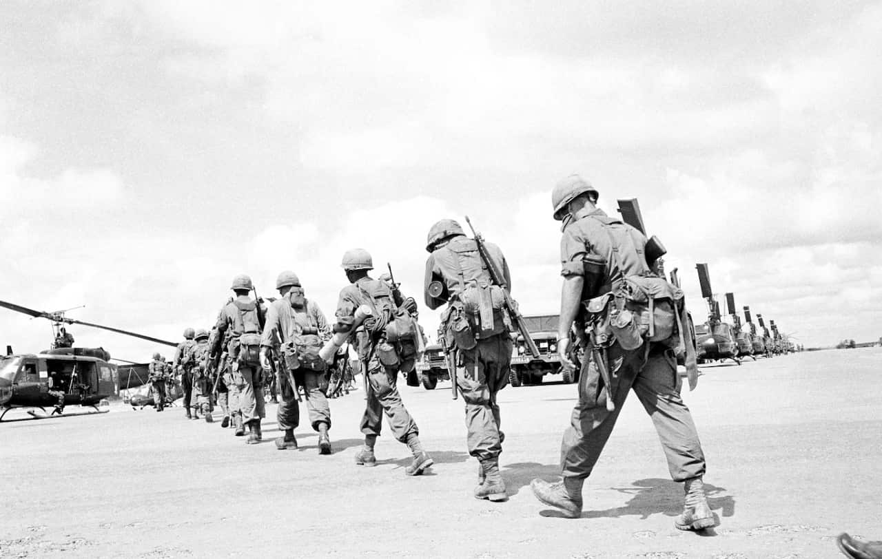 Paratroopers, heavily loaded with their packs, rations for several days and mortar ammunition walk in file across the Bien Hoa airfield, Vietnam in 1965.