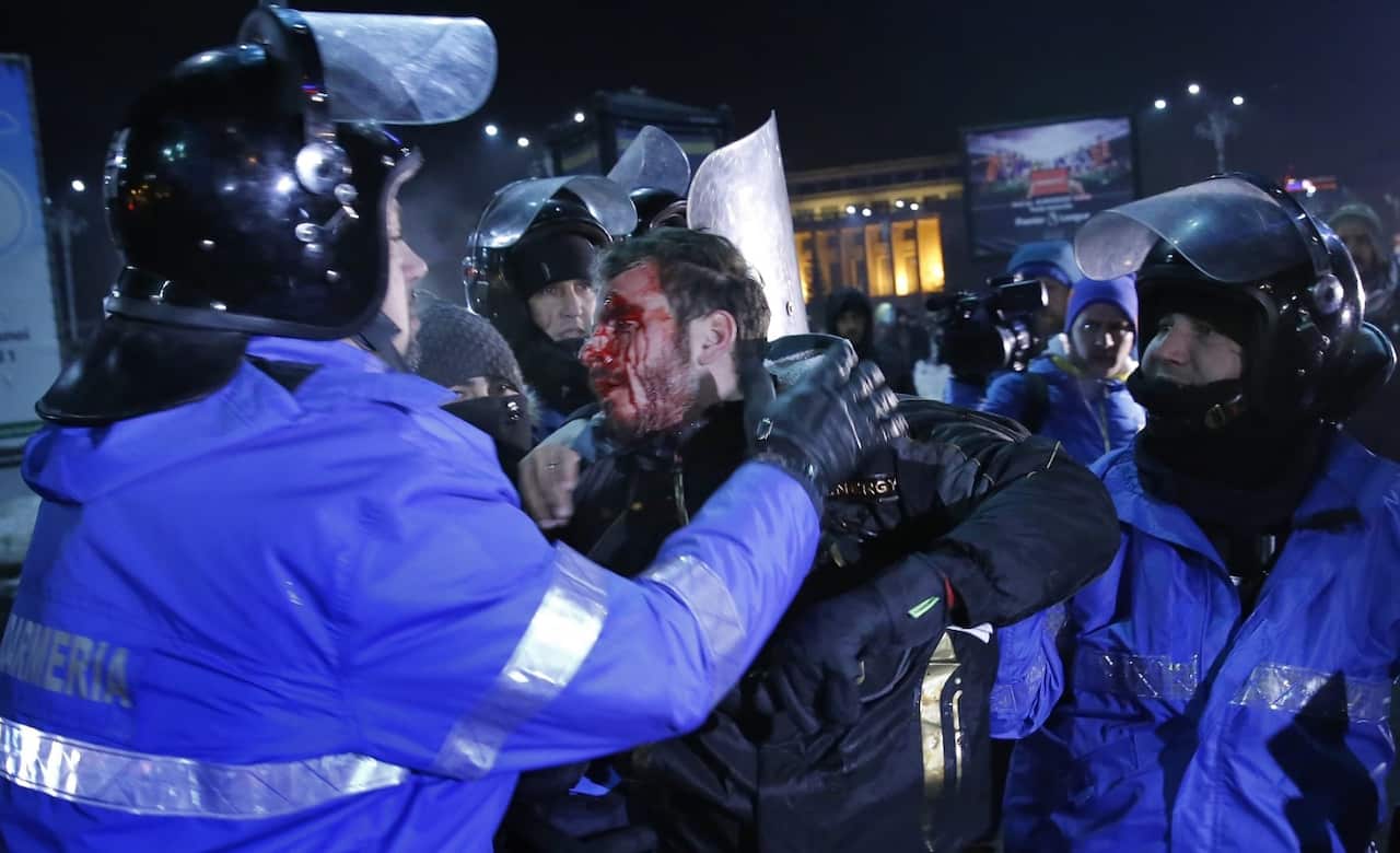 A wounded young man is arrested by the riot police during a protest rally in front of government headquarters in Bucharest (AAP)