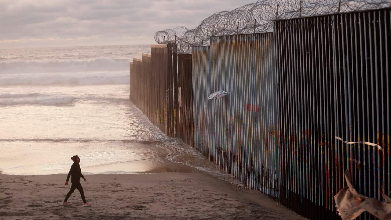A woman walks on the beach next to the border wall topped with razor wire in Tijuana, Mexico.