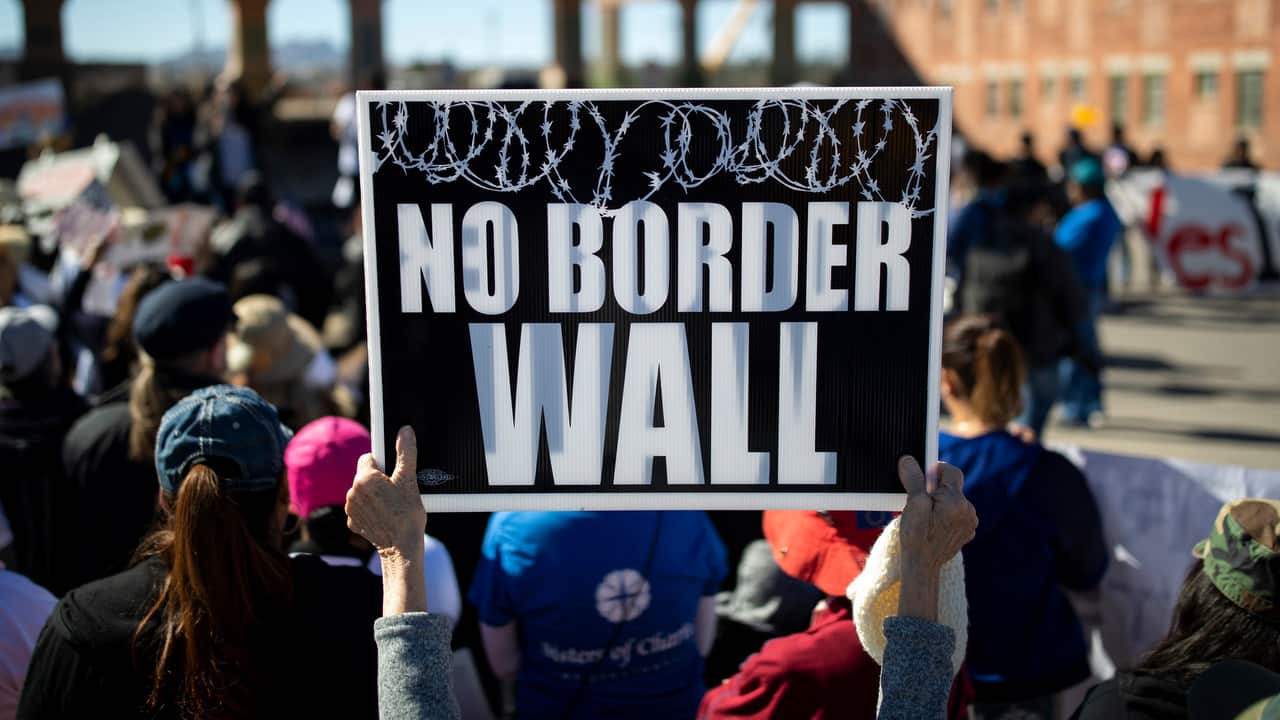 A protester holds a sign near the border after a group marched to protest a proposed wall being built along the border with Mexico in El Paso, Texas.