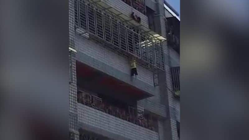 The boy is seen clinging to the security grill enclosure of the balcony on the fifth floor of an apartment building in Taiwan.