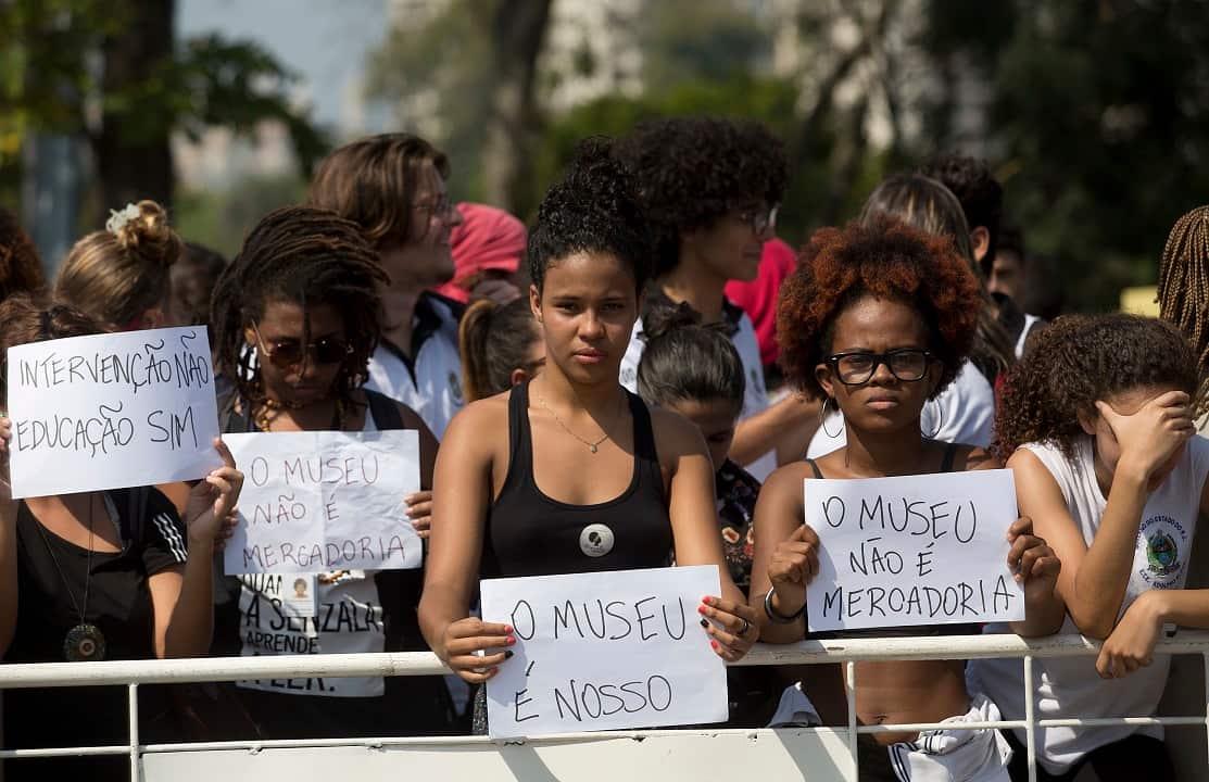 Protesters hold signs that read: "The museum is ours" and the "The museum is not merchandise."