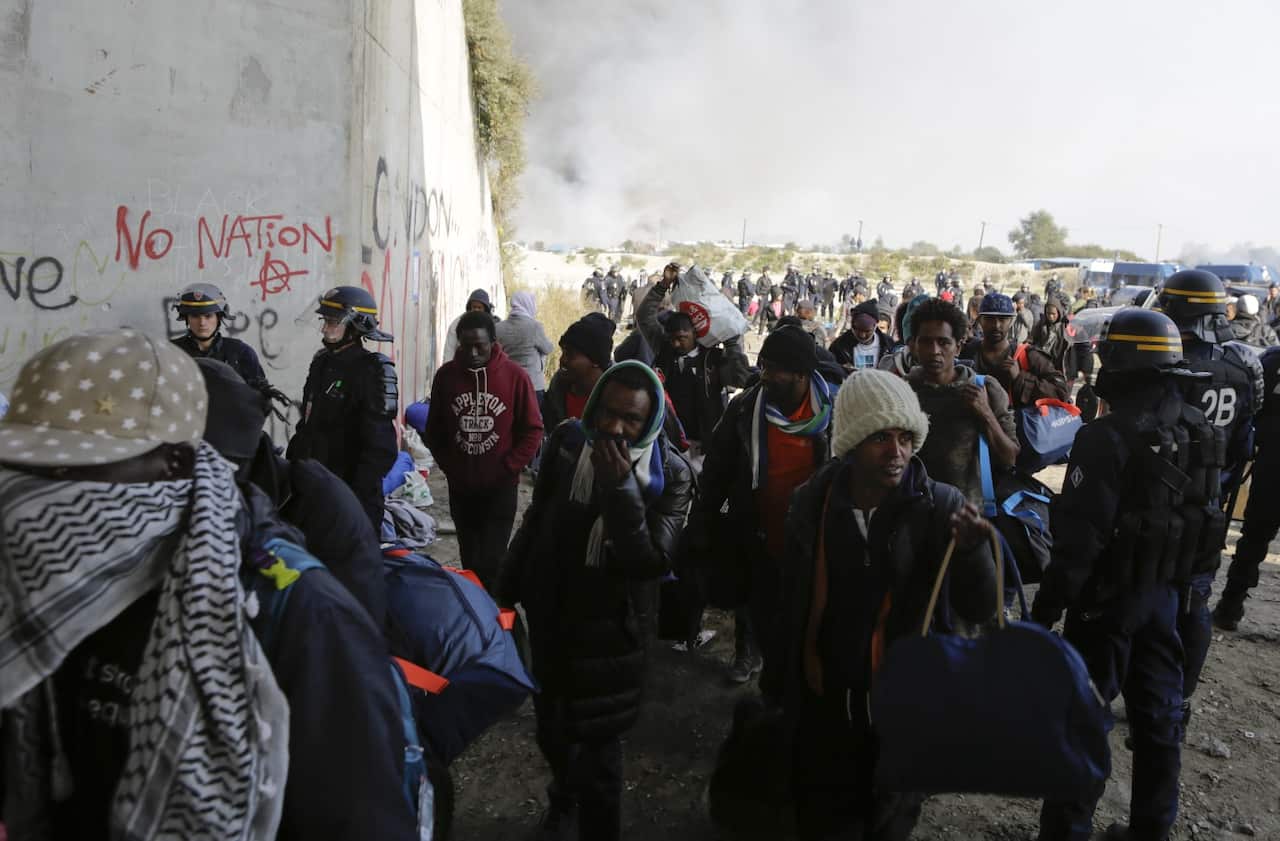 Migrants flee from smoke in the Jungle migrant camp in Calais after a fierce blaze cuts through a swathe of the camp overnight (AAP)