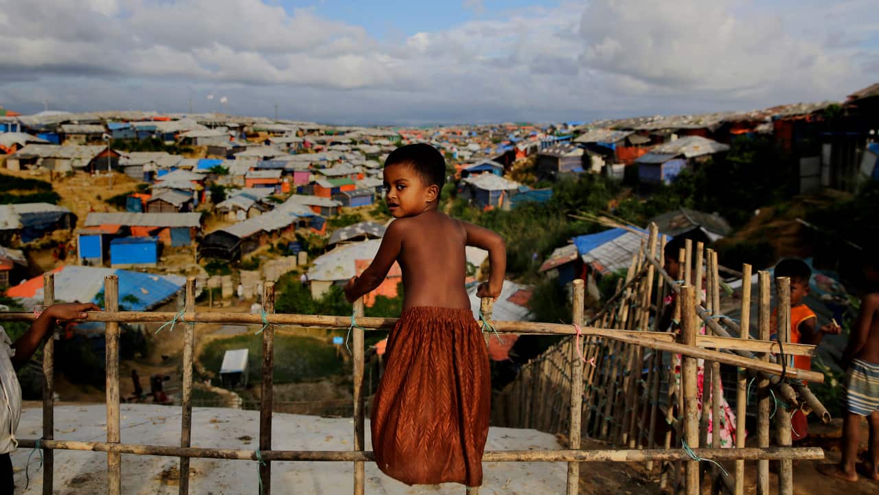 A Rohingya child stands on a bamboo fence overlooking an expanse of makeshift bamboo and tarp shelters at Kutupalong refugee camp.