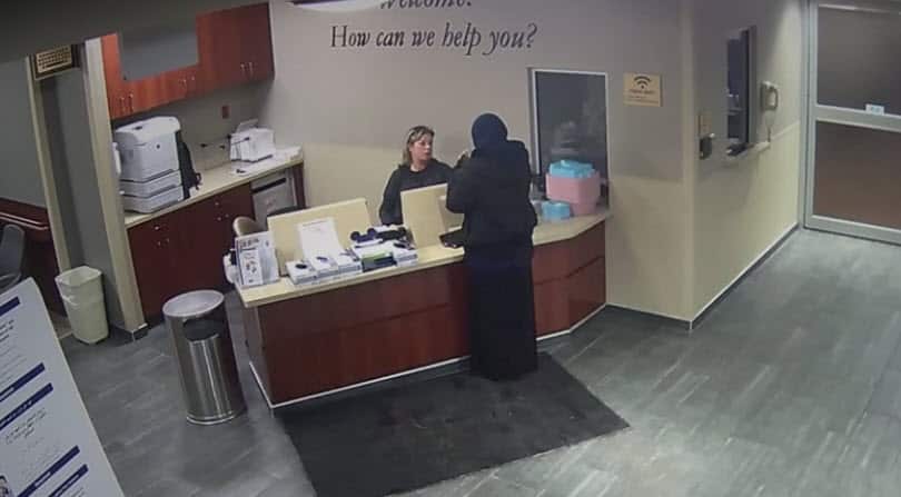 The woman arrives at the emergency room reception alone and can be seen talking to the receptionist. 