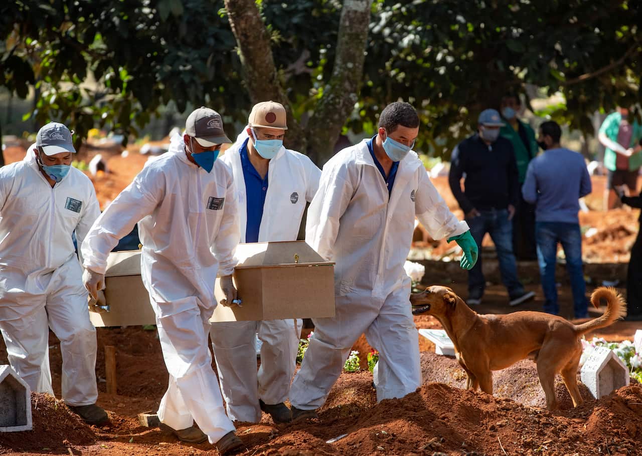 Cemetery workers in protective clothing carry a coffin (AAP)