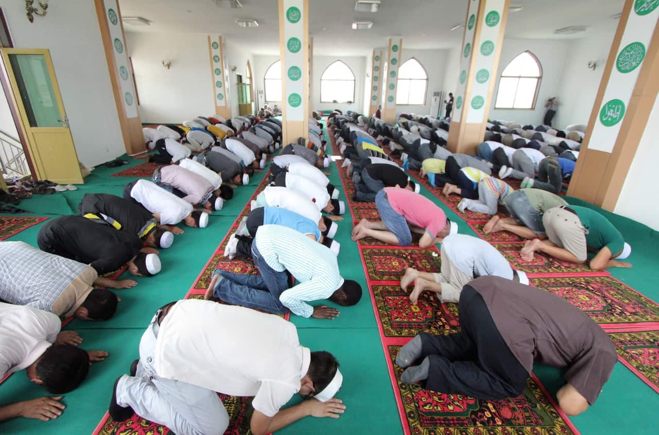 An African Muslim, center, kneels and bows among Chinese Muslims as they attend an Eid al-Fitr morning prayer
