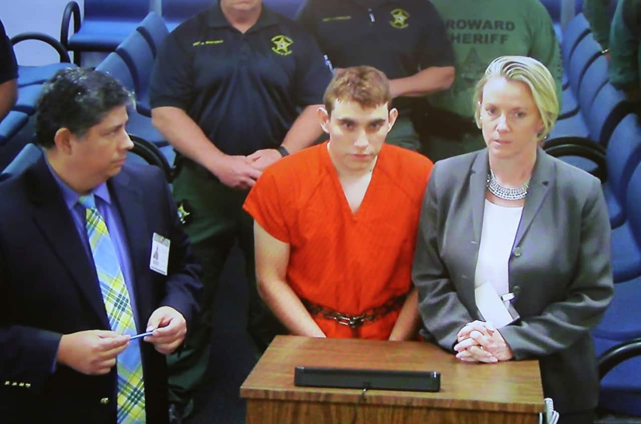 A video monitor shows school shooting suspect Nikolas Cruz, center, making an appearance before Judge Kim Theresa Mollica in Broward County Court