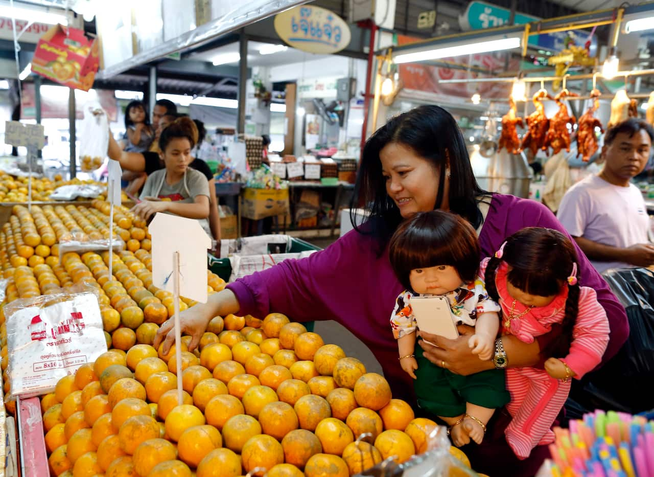 Thai devotee Ratchada Mahanavanont holding her Child Angels dolls as she looks for oranges at a market in Bangkok, Thailand.