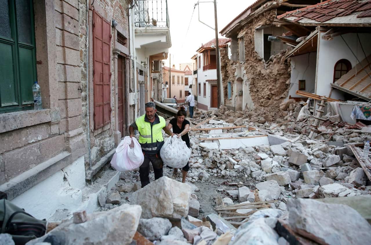 People carry their belongings amidst the rubble of collapsed houses in the village of Vrissas, following a strong earthquake struck Lesvos island