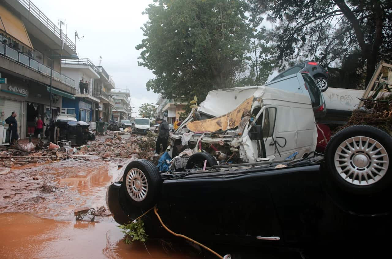 People inspect destroyed cars in flooded of mud roads in the centre of Mandra, western Attica, Greece, 15 November 2017 (AAP)