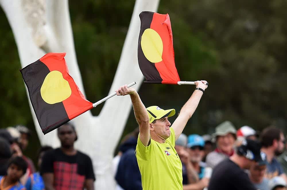 A goal umpire uses Aboriginal flags to signal a goal during a football match in Alice Springs in 2016.