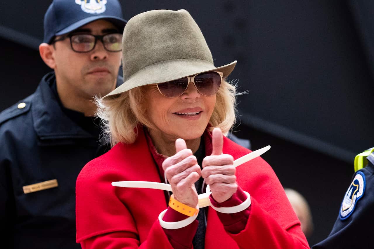 Fonda flashes the thumbs up as she's escorted away by police.