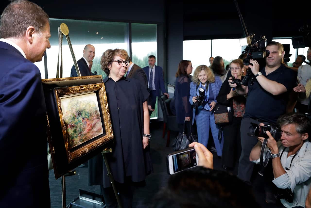 United States Attorney Geoffrey Berman, left, unveils a Renoir painting with Sylvie Sulitzer at a news conference, Wednesday, Sept. 12, 2018, in New York. 