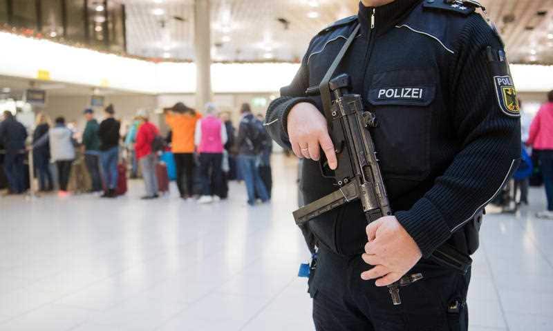 An armed federal police officer stands next to air passengers at the check-in desk at Hanover Airport.