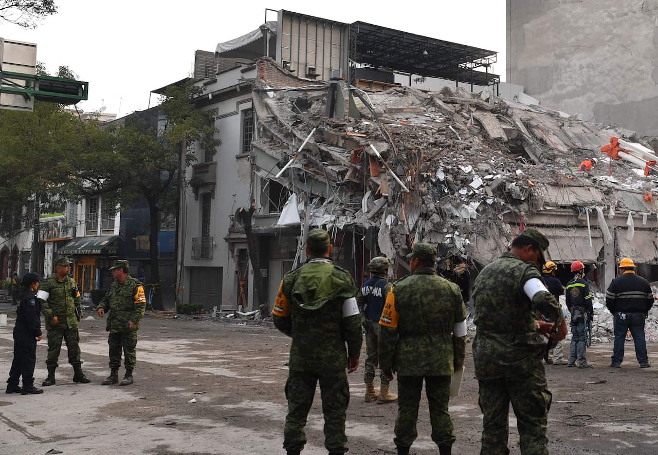 Rescuers, firefighters, policemen, soldiers and volunteers stand near a flattened building in Mexico City