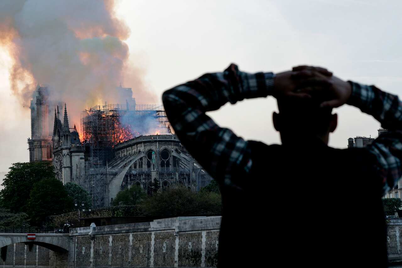 A man watches the landmark Notre-Dame Cathedral burn, engulfed in flames, in central Paris.