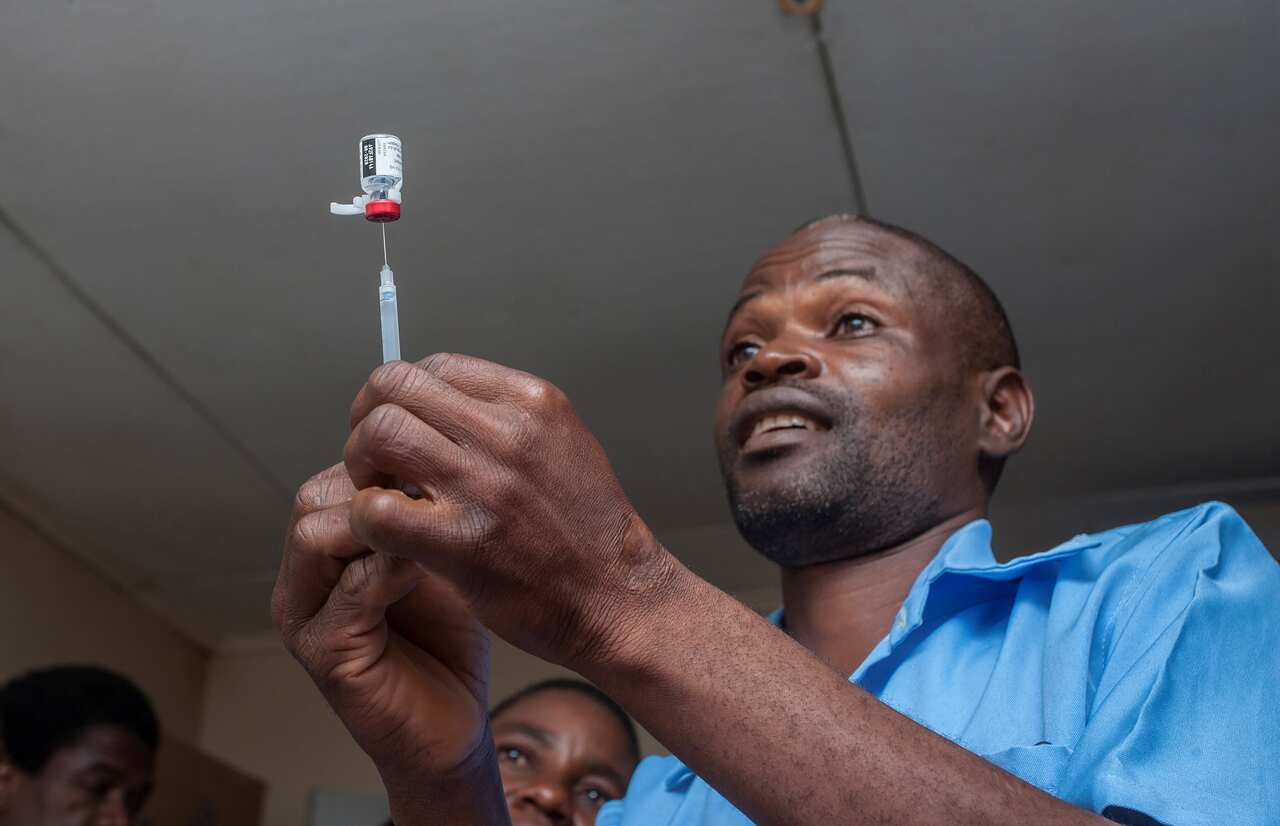 A health surveillance assistant (HAS) gets malaria vaccine from its bottle into an injection to be administered to a child.