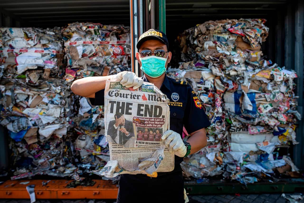 An Indonesian customs officer holds up a newspaper from a container filled with trash originating from Australia, which should have contained only waste paper.