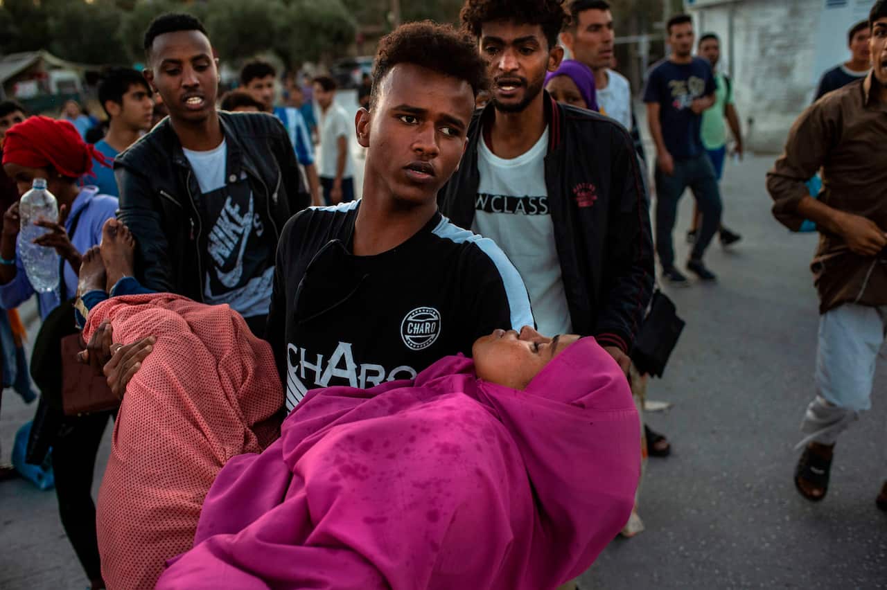 A migrant carries a woman during clashes with police outside the refugee camp of Moria on the Greek island of Lesbos, on September 29, 2019
