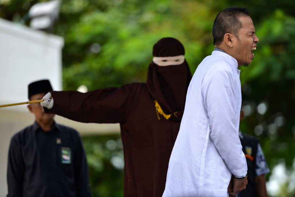 Aceh Ulema Council (MPU) member Mukhlis bin Muhammad reacts as he is whipped in public