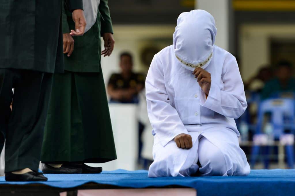 A woman prepares to be whipped in public by a member of the Sharia police in Banda Aceh on October 31, 2019