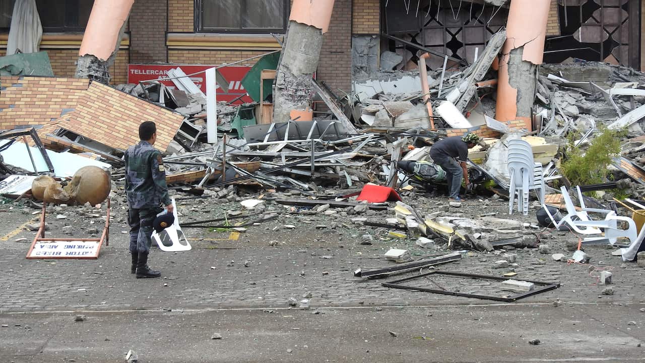 A policeman watches as a resident retrieves his motorcycle among the rubble of a damaged building.