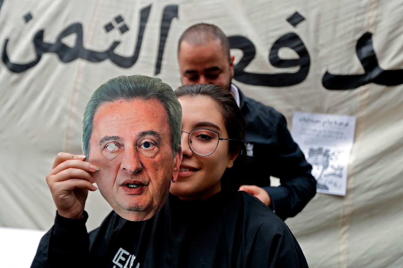A Lebanese anti-government protester holds a mask of Lebanon's Central Bank Governor Riad Salameh as she sits for a haircut in front of the central bank HQ.