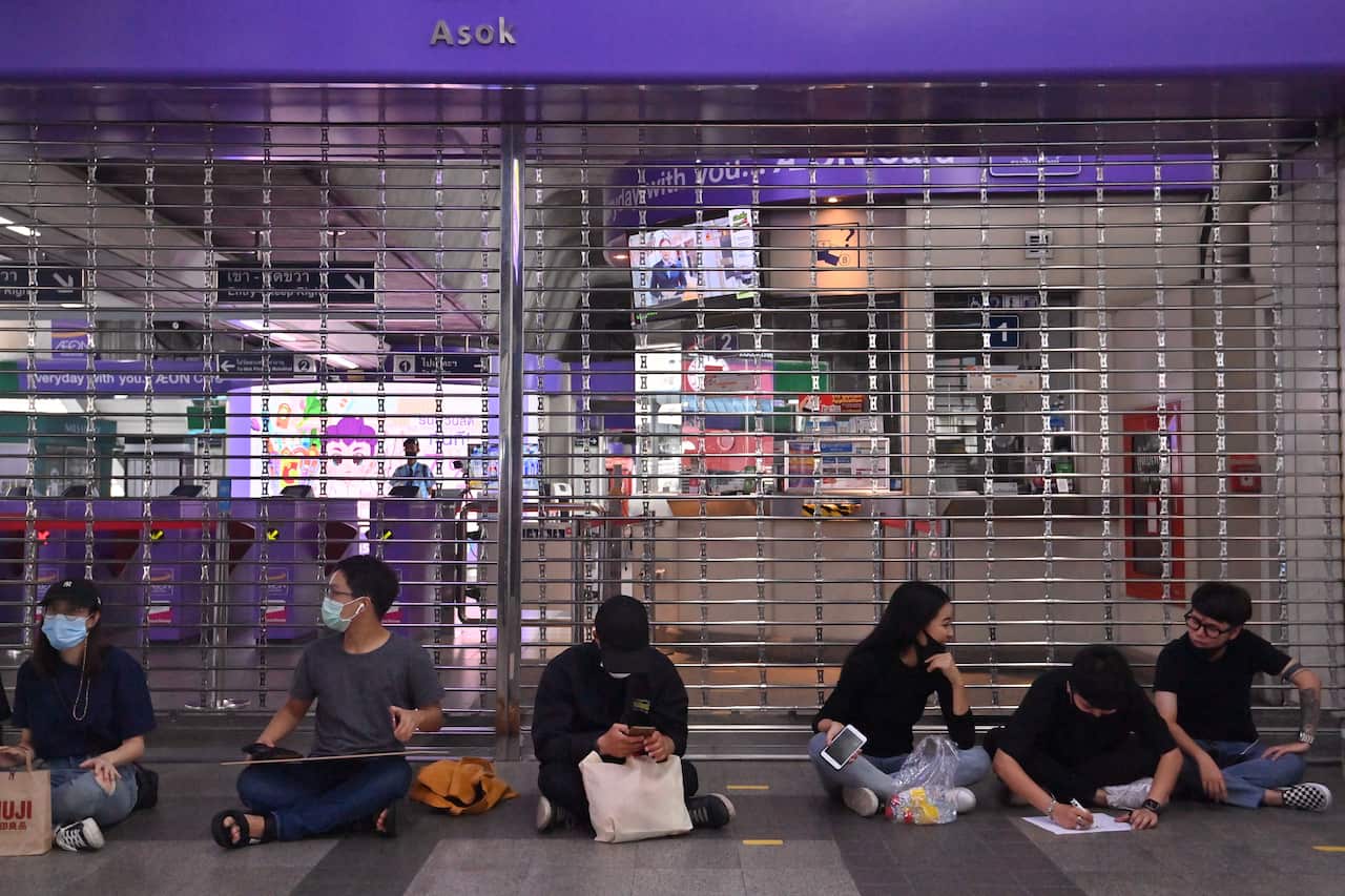 Pro-democracy protesters sit outside the Asok BTS skytrain station after it was closed ahead of a possible anti-government rally in Bangkok on 18 October. 