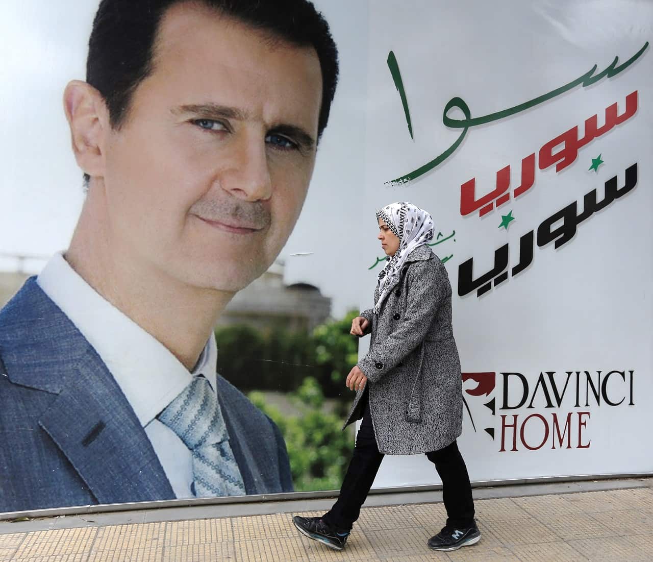A Syrian woman walks past a placard bearing a portrait of President Bashar al-Assad.