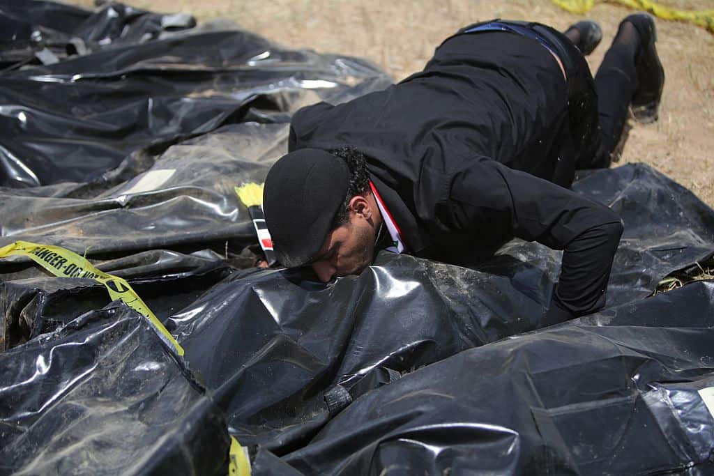 An Iraqi man kisses a body-bag lying amidst other bags containing the remains of people believed to have been slain by jihadists of the Islamic State (IS) group lie on the ground at the Speicher camp in the Iraqi city of Tikrit, on April 12, 2015. 