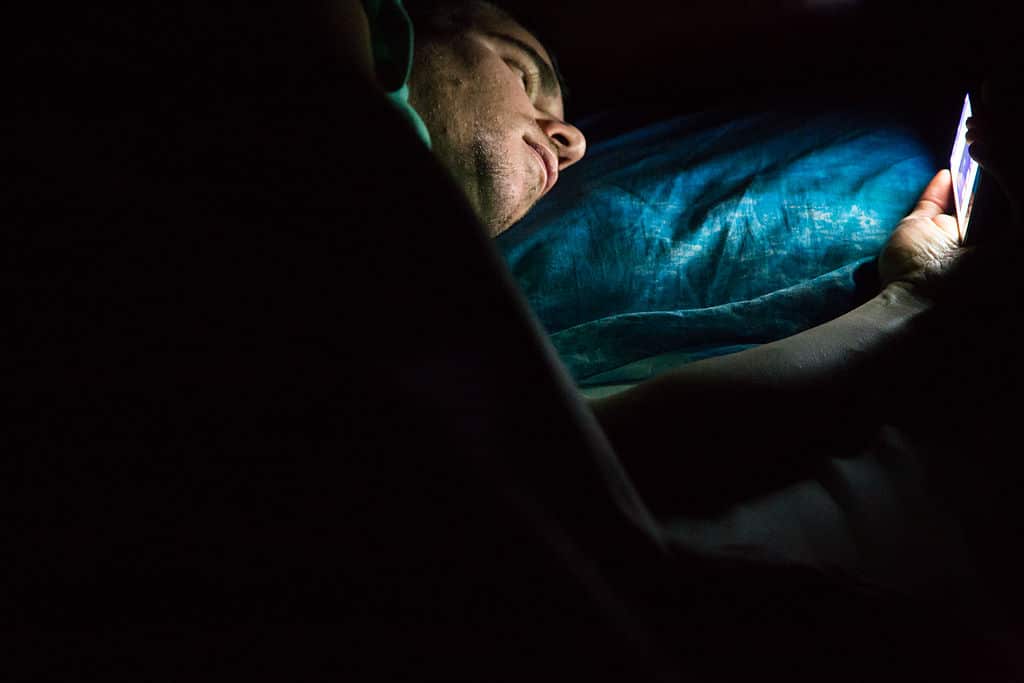 Man laying on bed at late night in a dark room checking his smartphone. 
