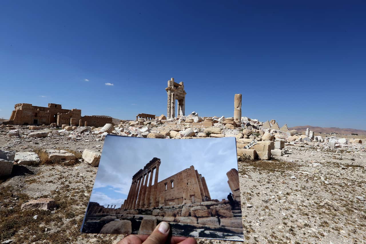 A general view taken on March 31, 2016 shows a photographer holding his picture of the Temple of Bel taken on March 14, 2014 in front of the remains of the historic temple after it was destroyed by Islamic State (IS) group jihadists in September 2015 in t