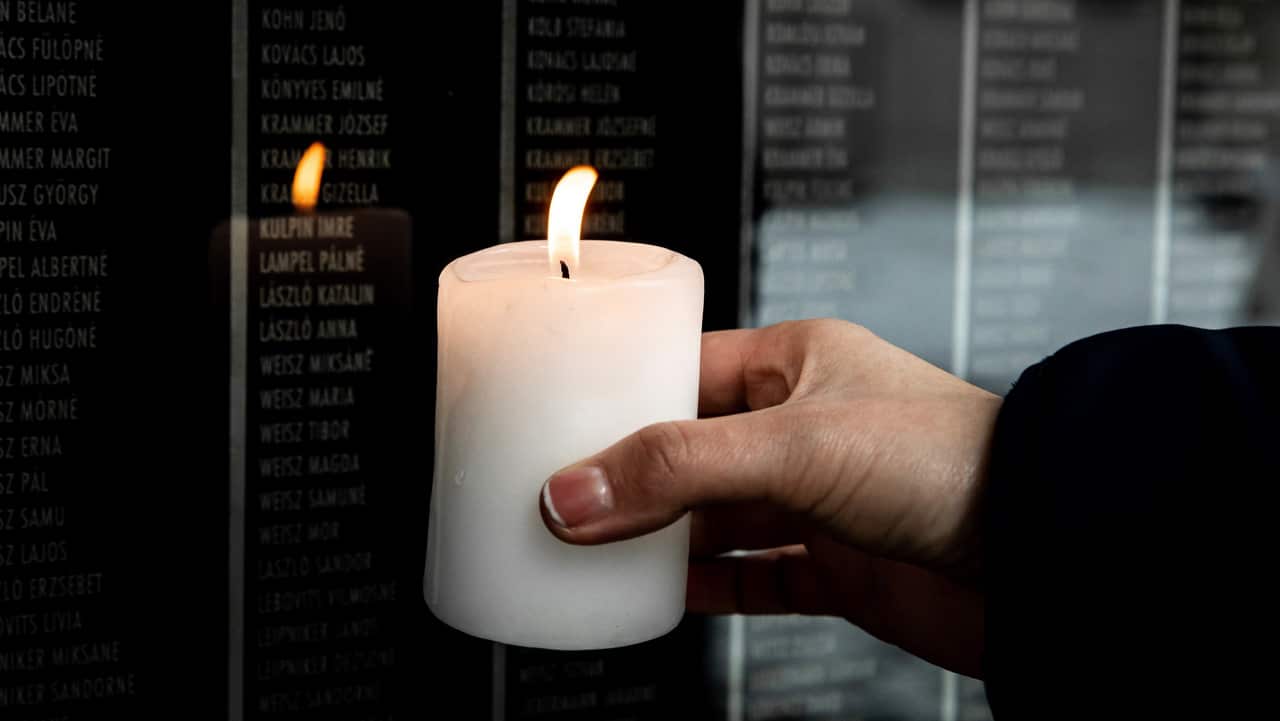 A visitor holds a burning candle by the victims' wall in the Holocaust Memorial Center.