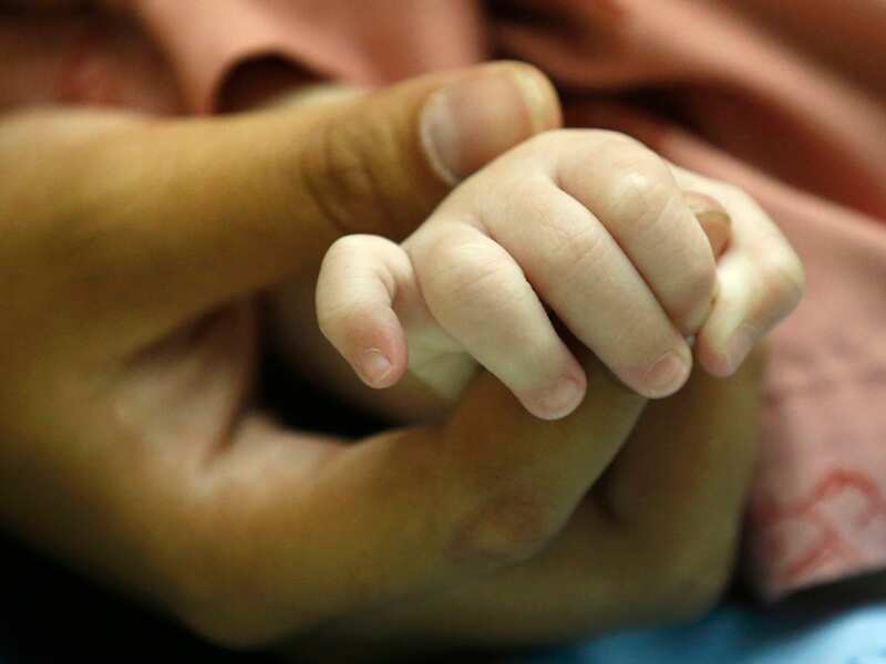 A surrogate mother holds the hand of a newborn baby.