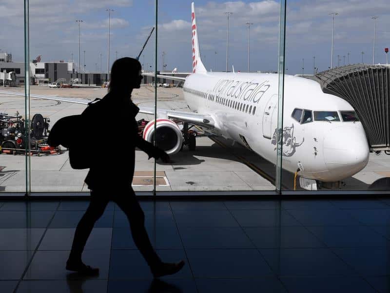 A person walking through an airport terminal. A plane a seen through the window they are walking past.