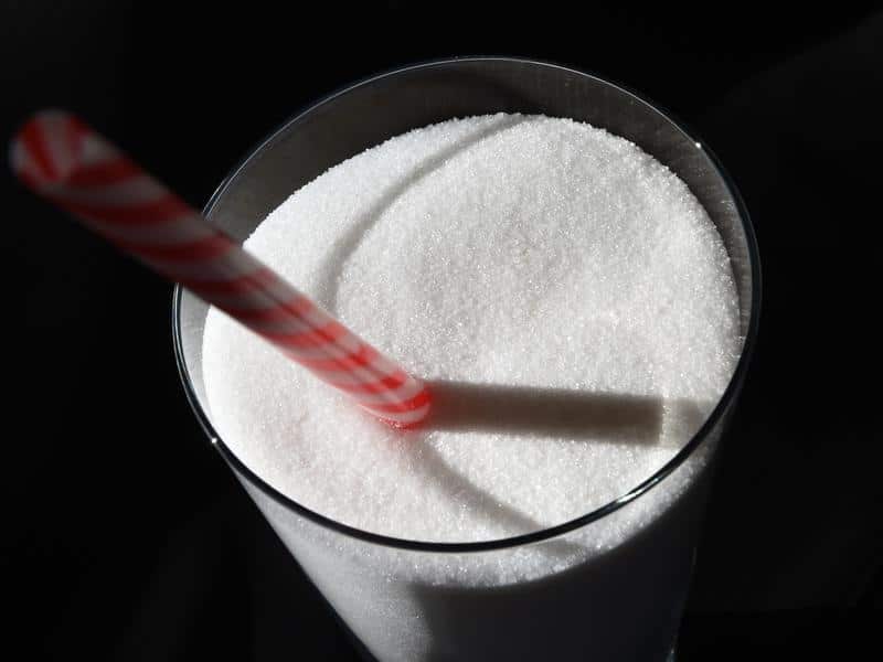 Image of white sugar in a glass with a drinking straw.