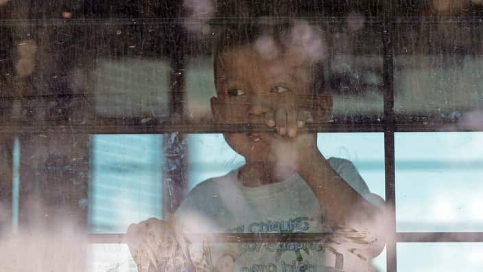 An immigrant child looks out from a US Border Patrol bus leaving as protesters fill the streets.