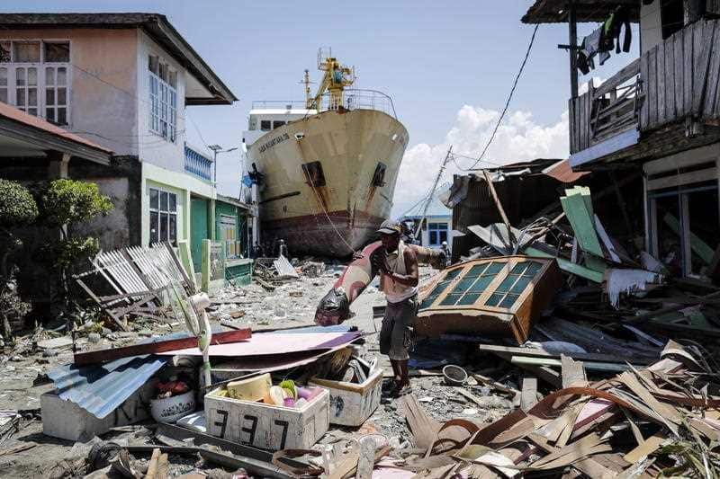 An Indonesian man carries his belongings past a stranded ship at a tsunami devastated area in Wani, Donggala, Central Sulawesi.