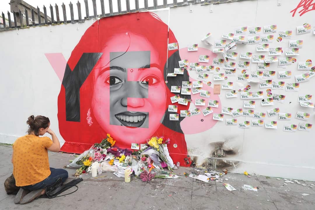 A woman kneels infront of a mural of Savita Halappanavar in Dublin.