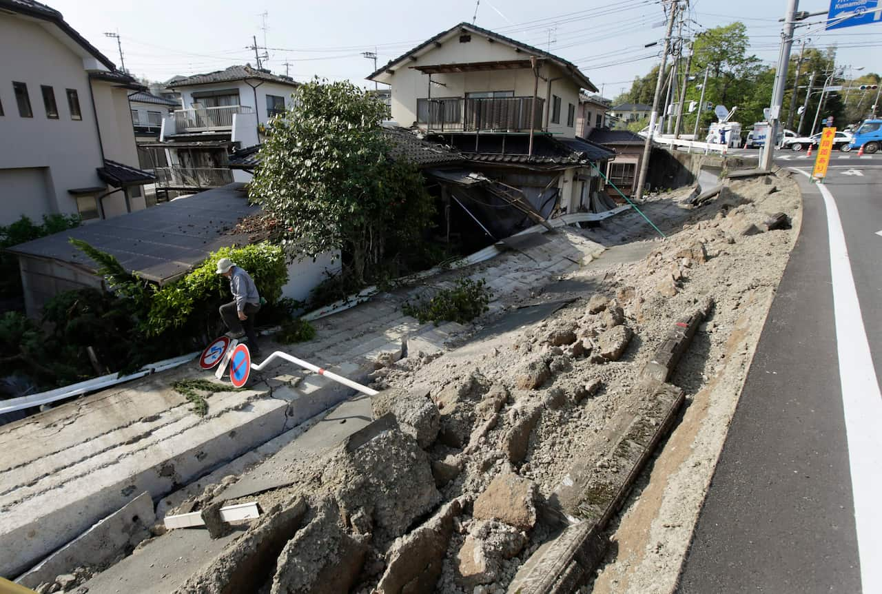 A resident leaps over a traffic sign after checking his house that was damaged by a collapsed national highway in the town of Mashiki, Japan