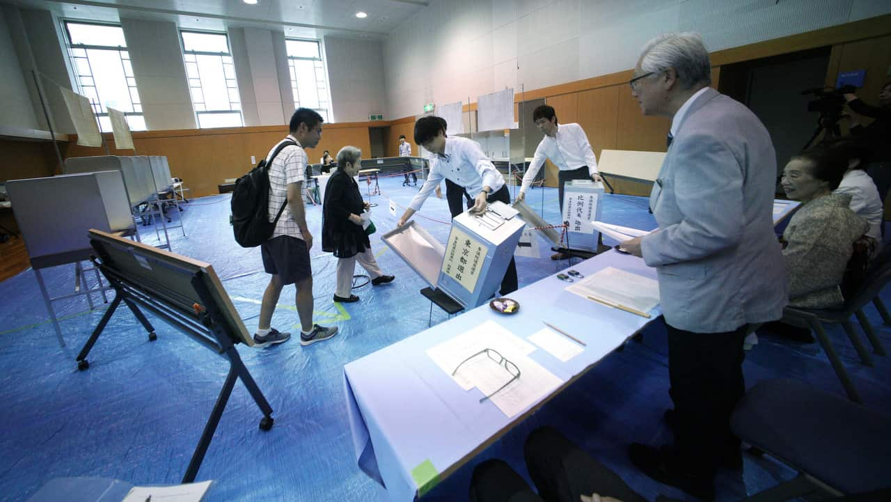 Representatives of a local election administration commission show the earliest two voters the empty ballot box before they cast their votes.